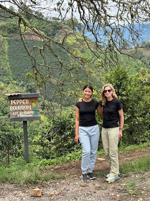 Ilse and anji hernandez standing on a dirt path with a 'Pepper Bourbon Lot 42' sign in a lush green landscape.