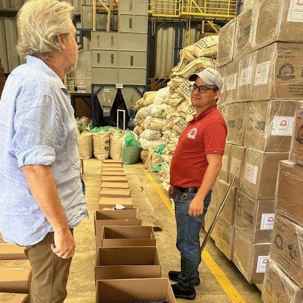 phillip and wilton benitez talking in the warehouse in front of a wall of boxes filled with specialty green beans
